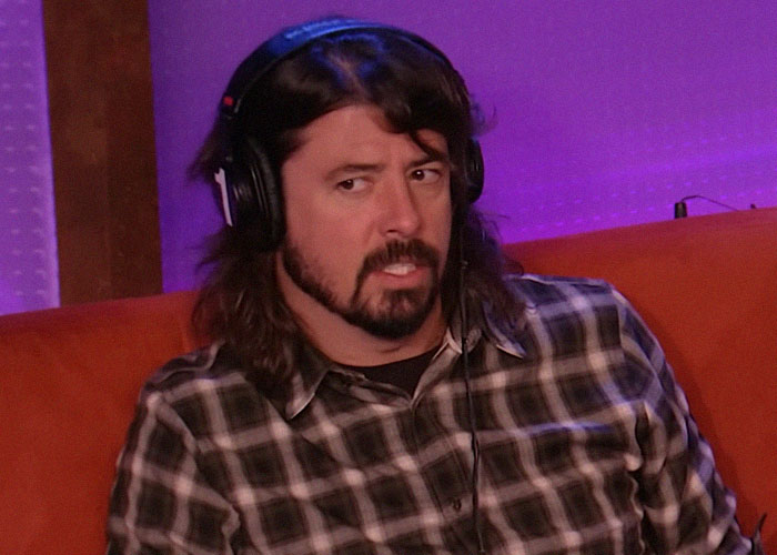 Hombre con auriculares, camisa a cuadros, sentado en un sofá naranja, representando traición en hollywood y momentos de engaño.