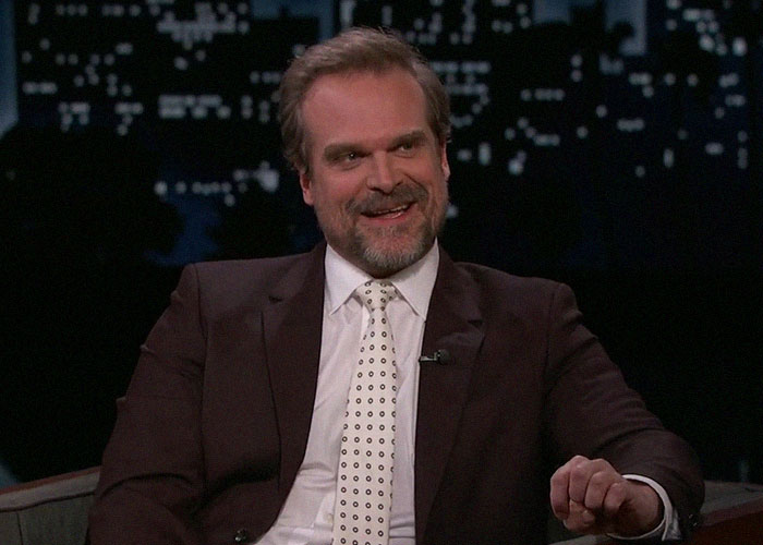 Hombre con traje oscuro y corbata blanca, sonriente en una entrevista, representando momentos de traición en Hollywood.