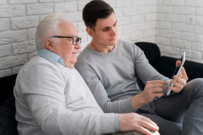 Young man showing his elderly father something on a smartphone, depicting secrets people refuse to reveal to their parents.