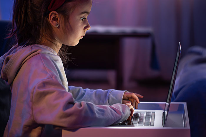 Young girl focused on laptop screen in dim room, illustrating deep secrets people refuse to reveal to their parents online.
