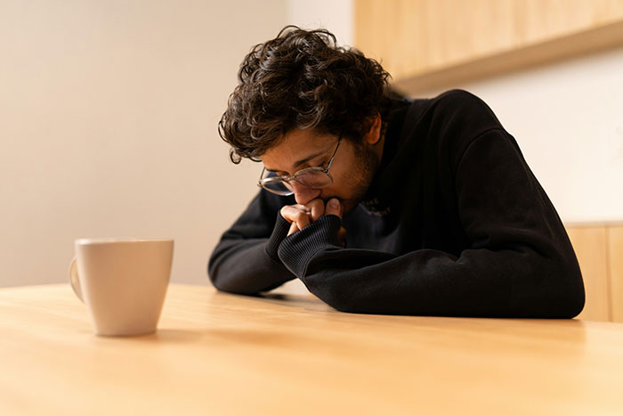 Young man with glasses sitting at a table deep in thought, reflecting on secrets people refuse to reveal to parents.