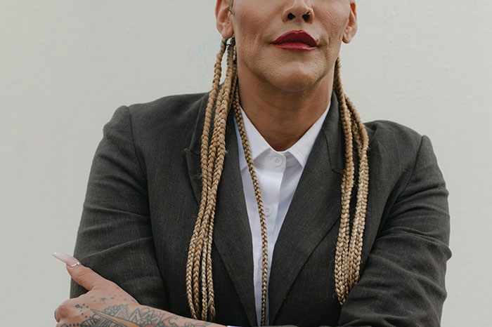 Person with braided hair and tattoos wearing a dark blazer, representing deepest secrets people refuse to reveal to parents.