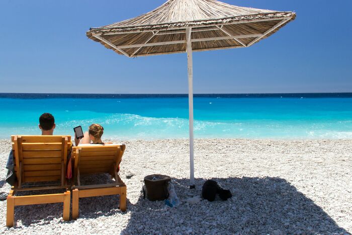 Two people relaxing on wooden chairs under a beach umbrella, enjoying peaceful mental and physical health benefits.