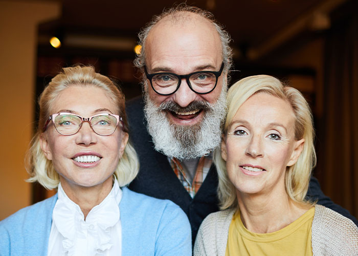 Three adults posing closely indoors, highlighting family dynamics during a holiday dinner with tension around engagement and lies.
