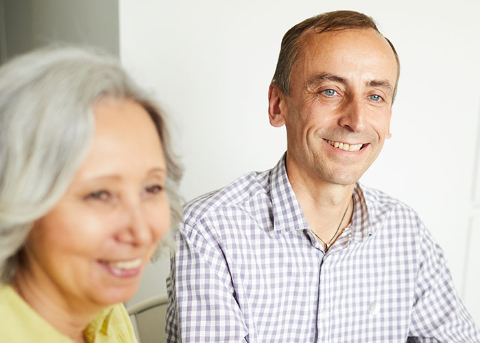 Smiling middle-aged couple during holiday dinner, woman rethinking engagement after fianc&eacute;&rsquo;s lie about her family.