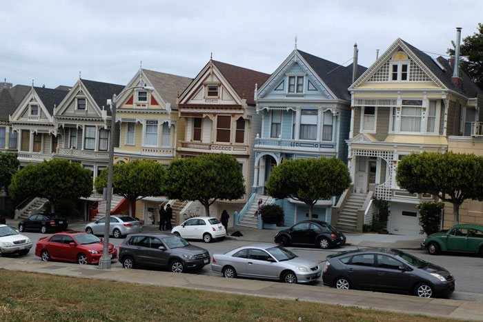 Victorian houses with cars parked along street, some blocking fire hydrant and driveway in residential neighborhood.