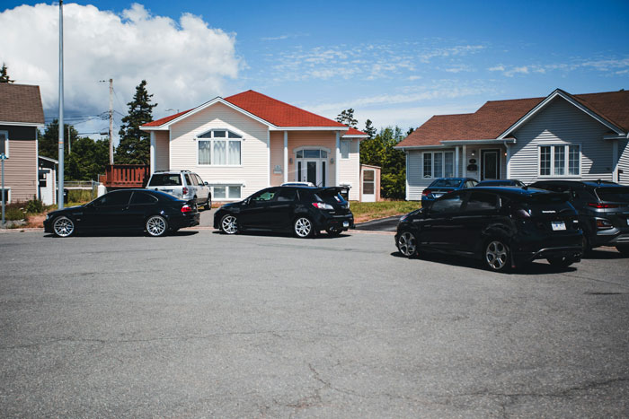 Several cars blocking a driveway and nearby fire hydrant in a suburban neighborhood on a clear day