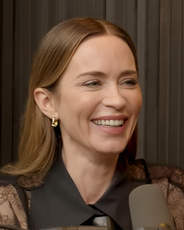 Emily Blunt smiling during a podcast recording, sparking rumors about plastic surgery and surgeon controversy.