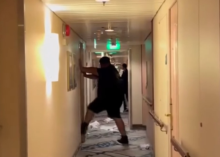 Man in dark clothing stumbling in narrow cruise ship hallway with scattered papers on the floor, cruise passenger incident scene.