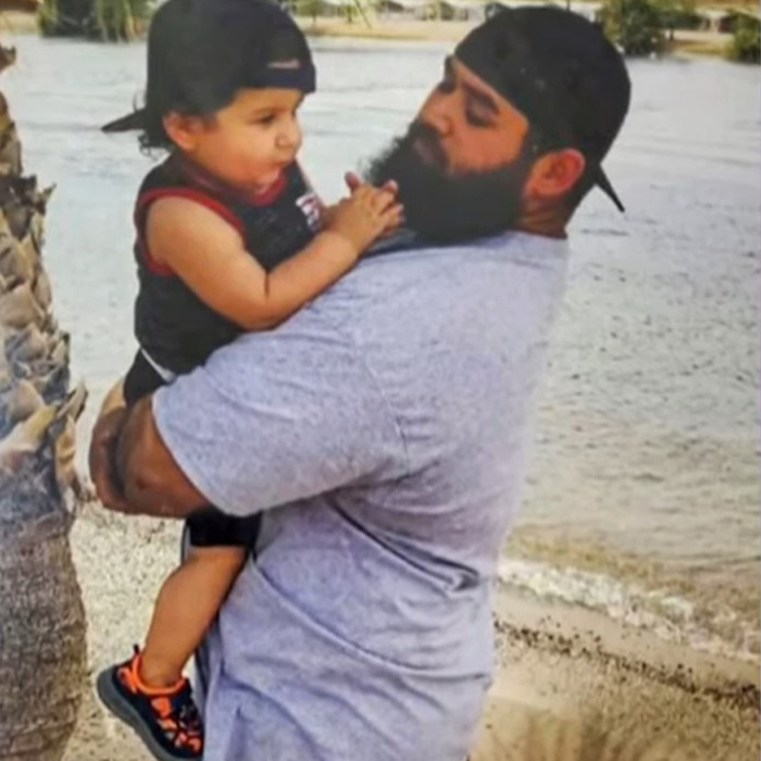 Man with a beard holding a child by the water, illustrating cruise passenger's body stuffed in fridge incident.