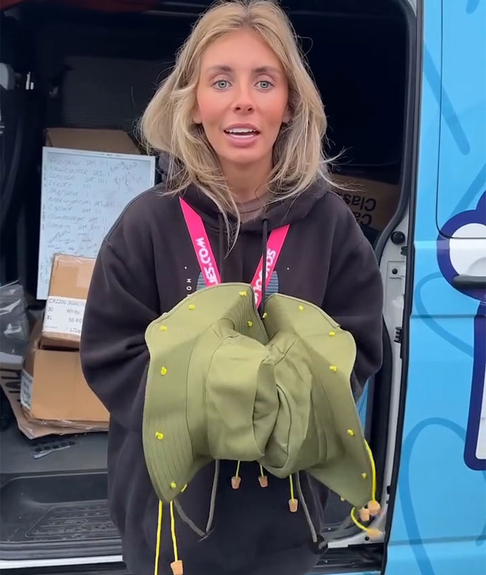 Blonde woman delivering Bonnie Blue's defiant message for authorities while holding green hats near a van in daylight.