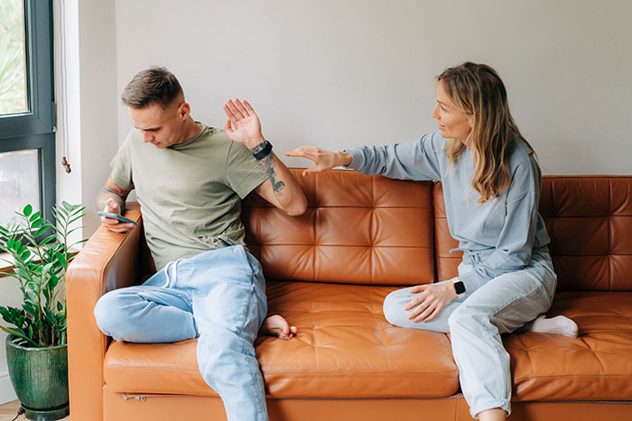 Woman confronting boyfriend on couch about cheating with astrology-obsessed friend, tension over Cancer zodiac sign discussed.