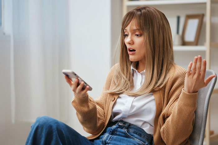 Young woman reacting with surprise while looking at phone, possibly frustrated with boyfriend editing face every photo.