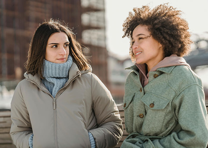 Two women talking outdoors, illustrating a man losing his girlfriend over a girl at work being nice to him.