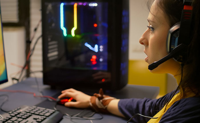 Young woman wearing headphones, focused on playing video games to unwind while seated at a gaming PC setup.