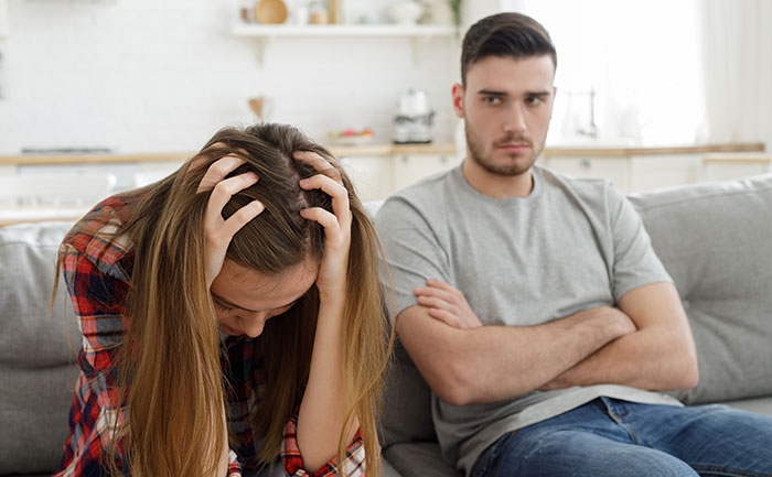 A frustrated couple sitting on a couch, guy mocking girlfriend for playing video games to unwind and saying it isn&rsquo;t ladylike.