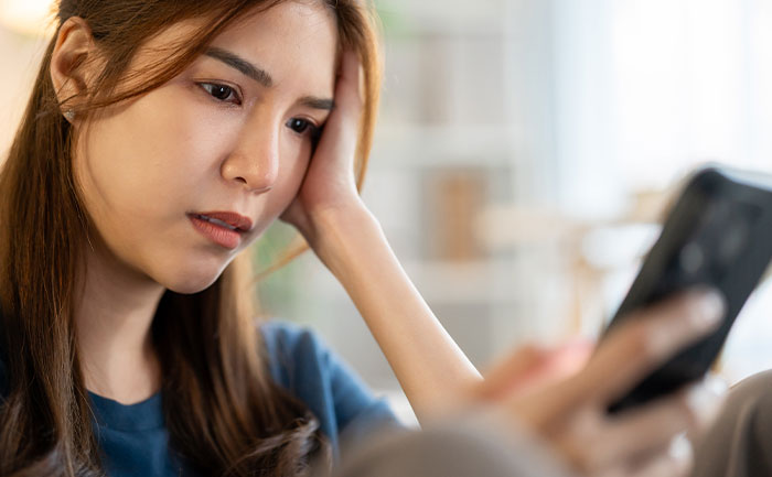 Young woman looking concerned while holding a smartphone, reflecting on a guy mocking girlfriend for playing video games.