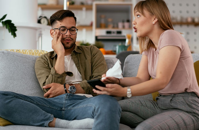 Couple having a tense conversation on couch, guy mocking girlfriend for playing video games to unwind and not being ladylike.