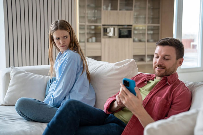 Angry girlfriend looks horrified while boyfriend scrolls phone on couch, tense moment about a racist gift.