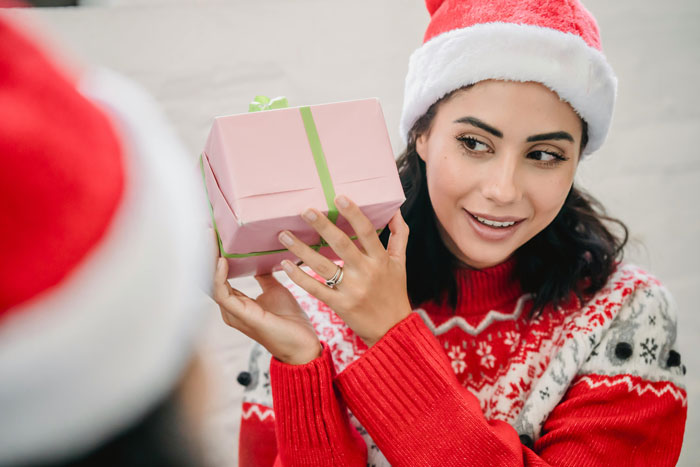 Woman in Santa hat holding pink present, uneasy expression, concept of racist gift and holiday tension