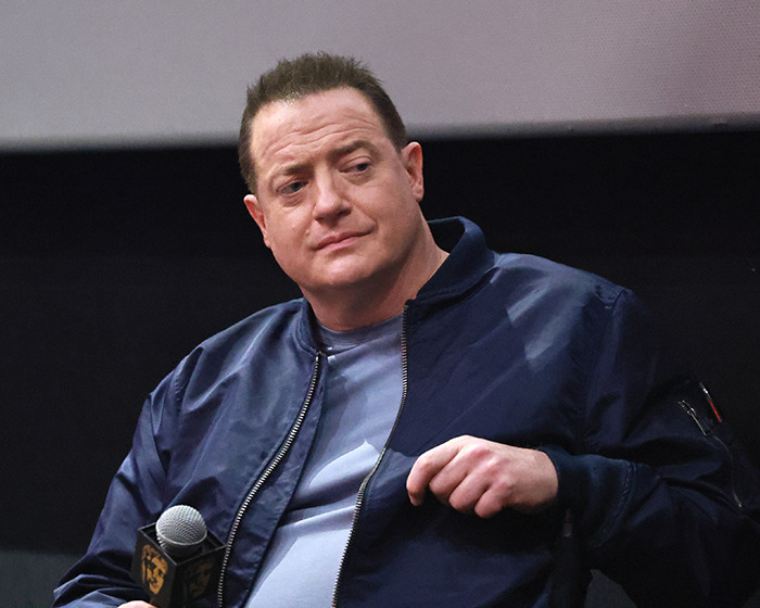 Brendan Fraser wearing a navy jacket, holding a microphone, sharing heartbreaking truth about his career after Oscar victory.