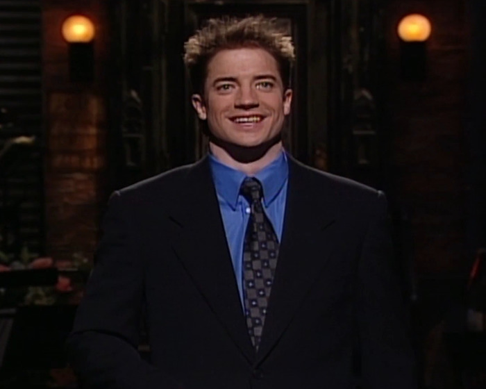 Brendan Fraser smiling in a dark suit and blue shirt, sharing a heartbreaking truth about his career after Oscar victory.