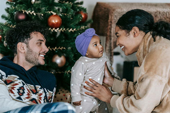 Woman welcoming her brother&rsquo;s family during holiday season with a baby near decorated Christmas tree indoors.