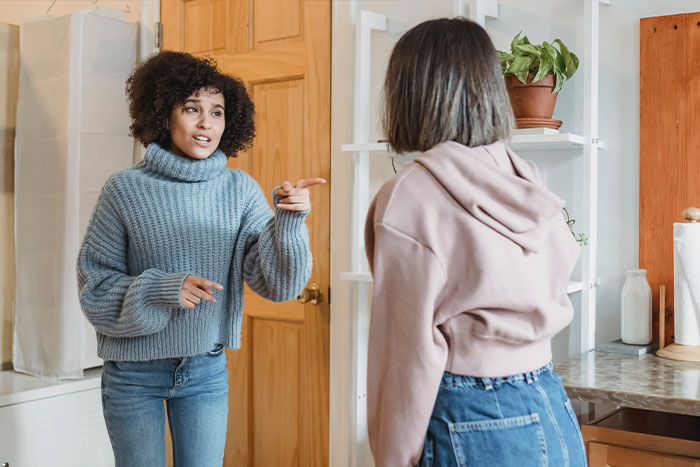 Two women in a kitchen having a tense conversation, depicting a woman welcoming her brother&rsquo;s family and complaints.