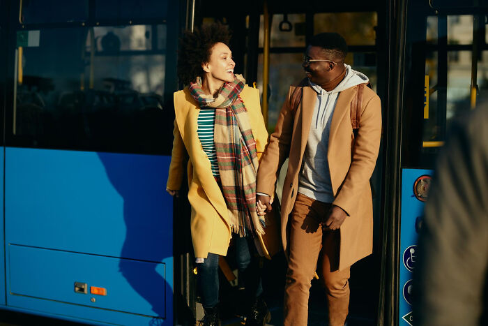 Young couple holding hands and smiling while stepping off a bus, illustrating small decisions with unexpected life-altering consequences.