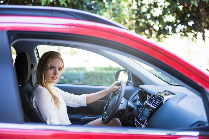 Young woman in white shirt sitting in red car holding steering wheel, symbolizing small decisions with life-altering consequences