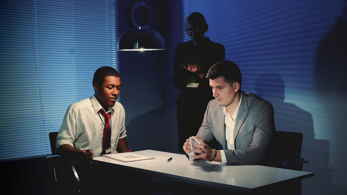Two men in a dim room make small decisions during an intense discussion, highlighting unexpected life-altering consequences.