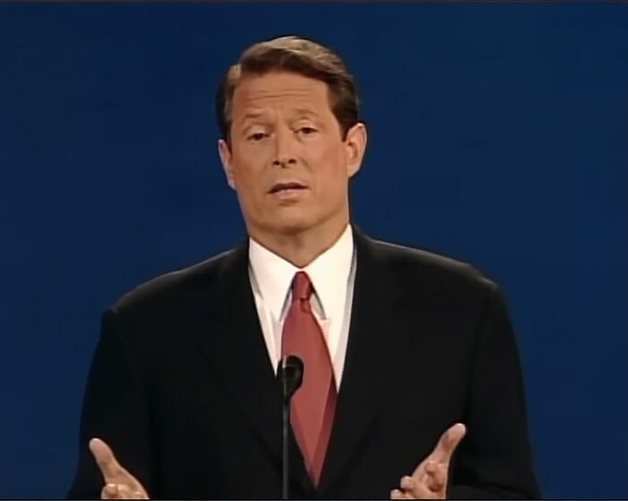 Man in a black suit and red tie speaking at a podium, illustrating stories of small decisions with life-altering consequences.