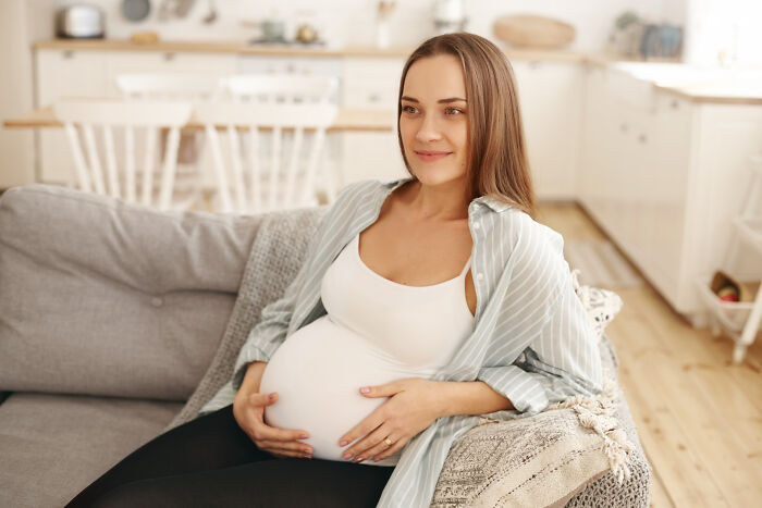 Pregnant woman sitting on a couch, reflecting on small decisions that led to unexpected life-altering consequences.