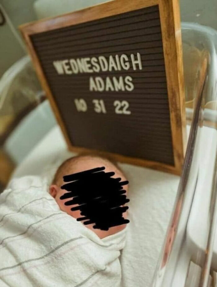 Newborn baby swaddled in a blanket lying in a hospital bassinet next to a sign, illustrating modern parenting trends.