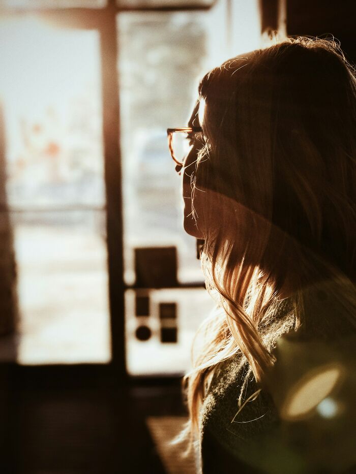 Woman with glasses looking out a window in soft light, reflecting on canceling her wedding two months before the big day