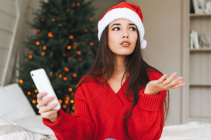 Young woman in a Santa hat and red sweater looking frustrated during Christmas dinner planning with lazy relatives and pizza options.