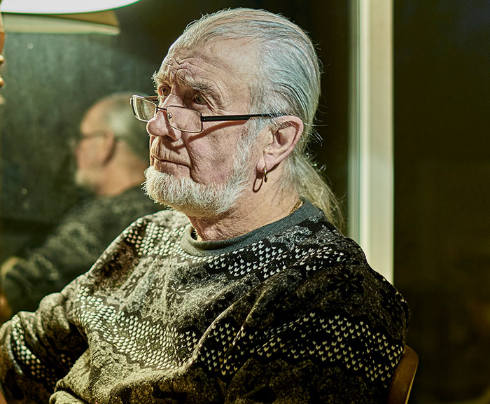 Elderly man with glasses and earring looking pensive, reflecting on guy kicking siblings out after surprise reveal.