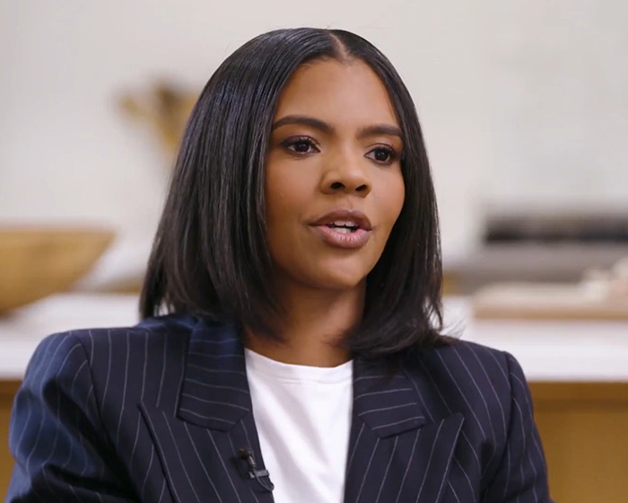 Erika Kirk speaking in an interview setting, wearing a dark pinstripe blazer and white top, discussing controversy.