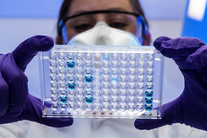 Scientist wearing mask and gloves holding a clear tray with blue liquid samples, illustrating disturbing science facts.