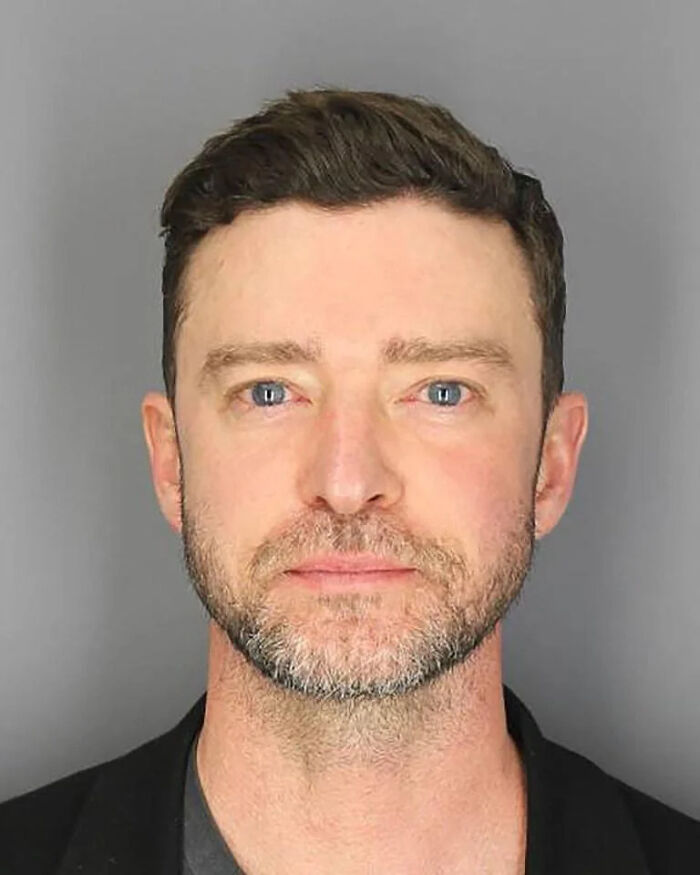 Close-up mugshot of a blue-eyed man with short dark hair and a beard after being arrested, part of celeb mugshots collection.