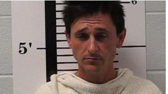 Male celebrity in a mugshot photo taken after being arrested, standing against a height measurement background.