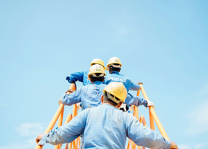 Workers wearing helmets and blue uniforms climbing an orange metal staircase at a construction site under clear sky.