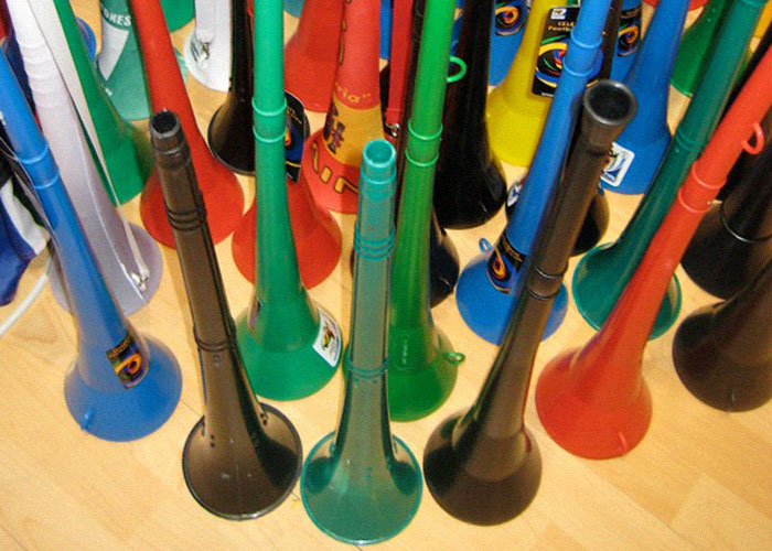 Colorful vuvuzelas scattered on a wooden floor, creating a chaotic scene of noise and disorder.