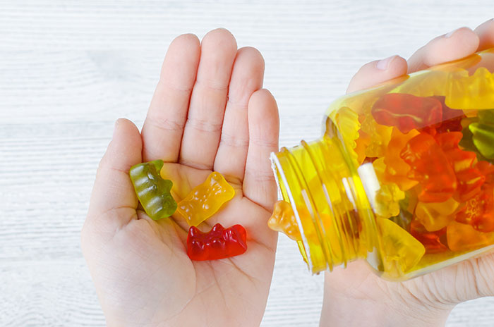 Hand holding colorful gummies poured from a yellow bottle, illustrating mom calls 911 after kids eat her gummies controversy.