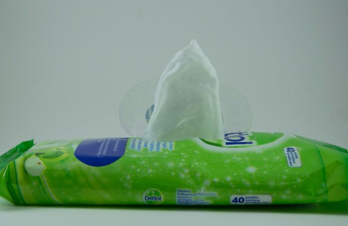 Green pack of wet wipes with an opened lid and one wipe partially pulled out showing small design mistakes in packaging.