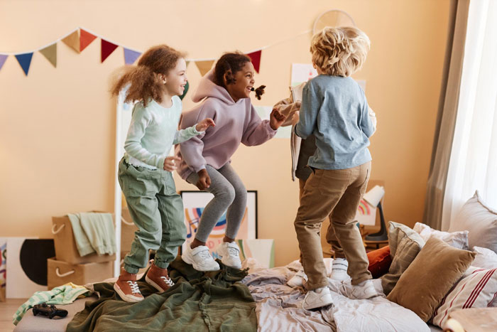 Three unruly kids jumping on a bed in a colorful room, illustrating chaos around no Christmas gifts from aunt.