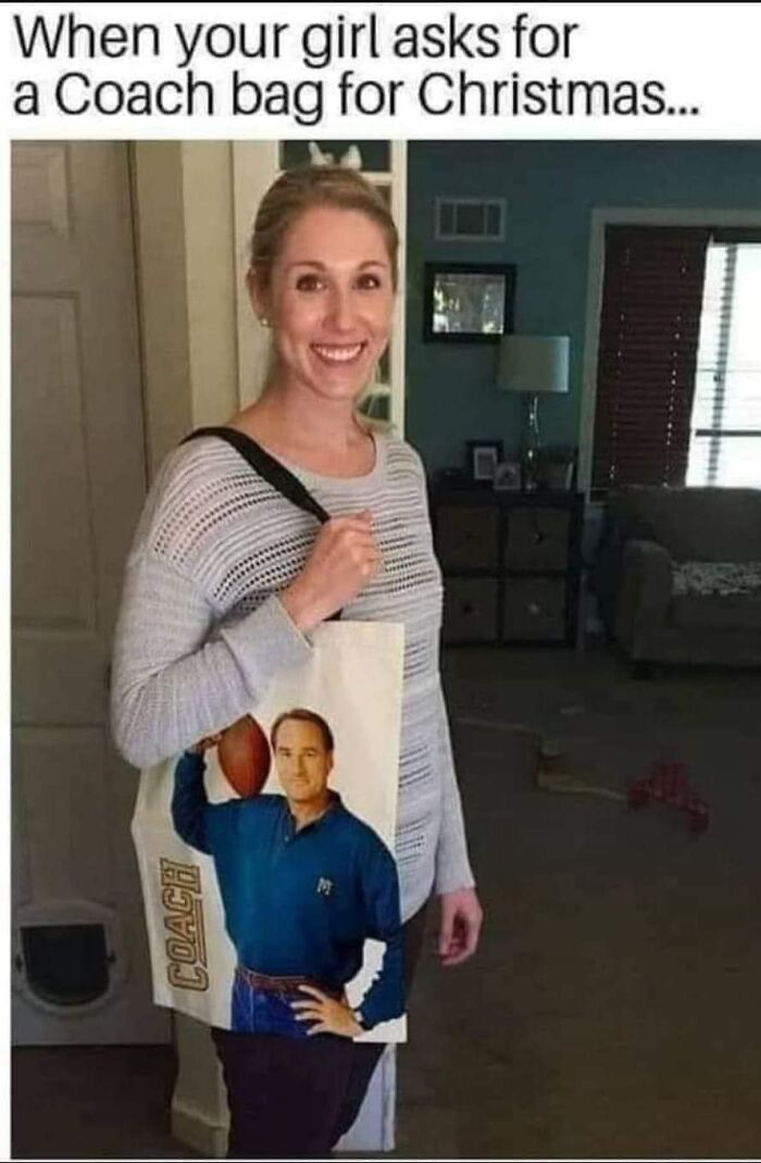 Woman smiling indoors holding a humorous coach-themed tote bag as a funny Christmas meme gift idea.