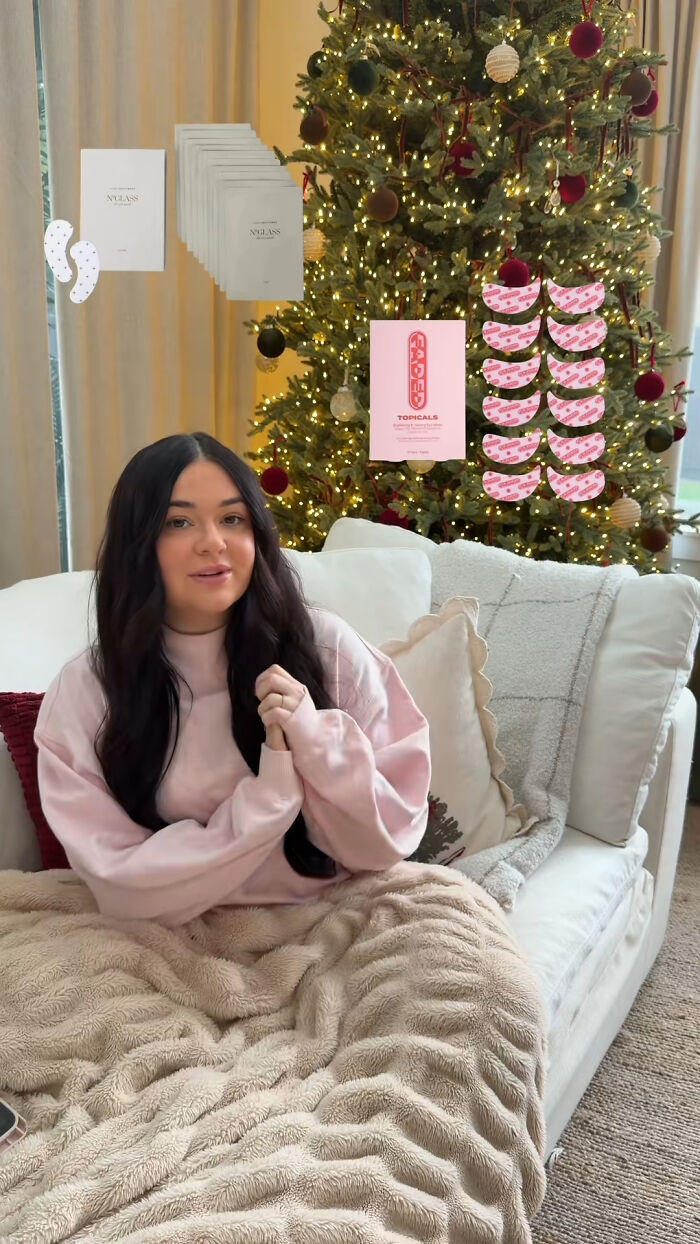 Woman sitting on couch by Christmas tree, sharing popular Christmas gifts that people highly recommend.