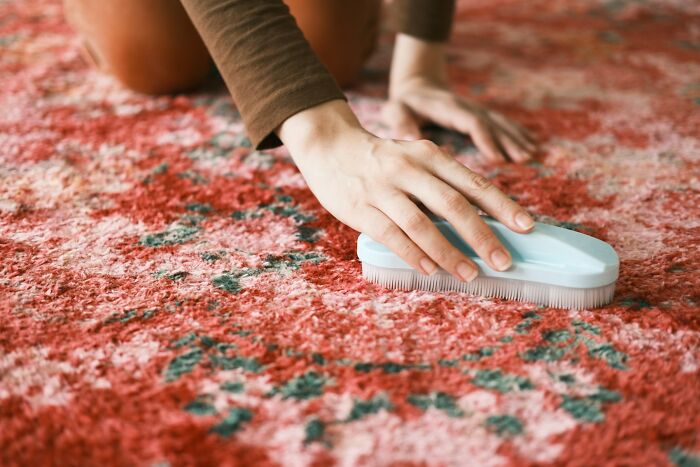 Person cleaning a red patterned carpet with a brush, related to work Christmas parties wildest stories cleanup.