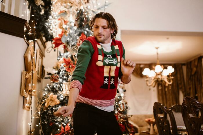 Man wearing an ugly sweater dancing by a decorated Christmas tree during a wild work Christmas party celebration.